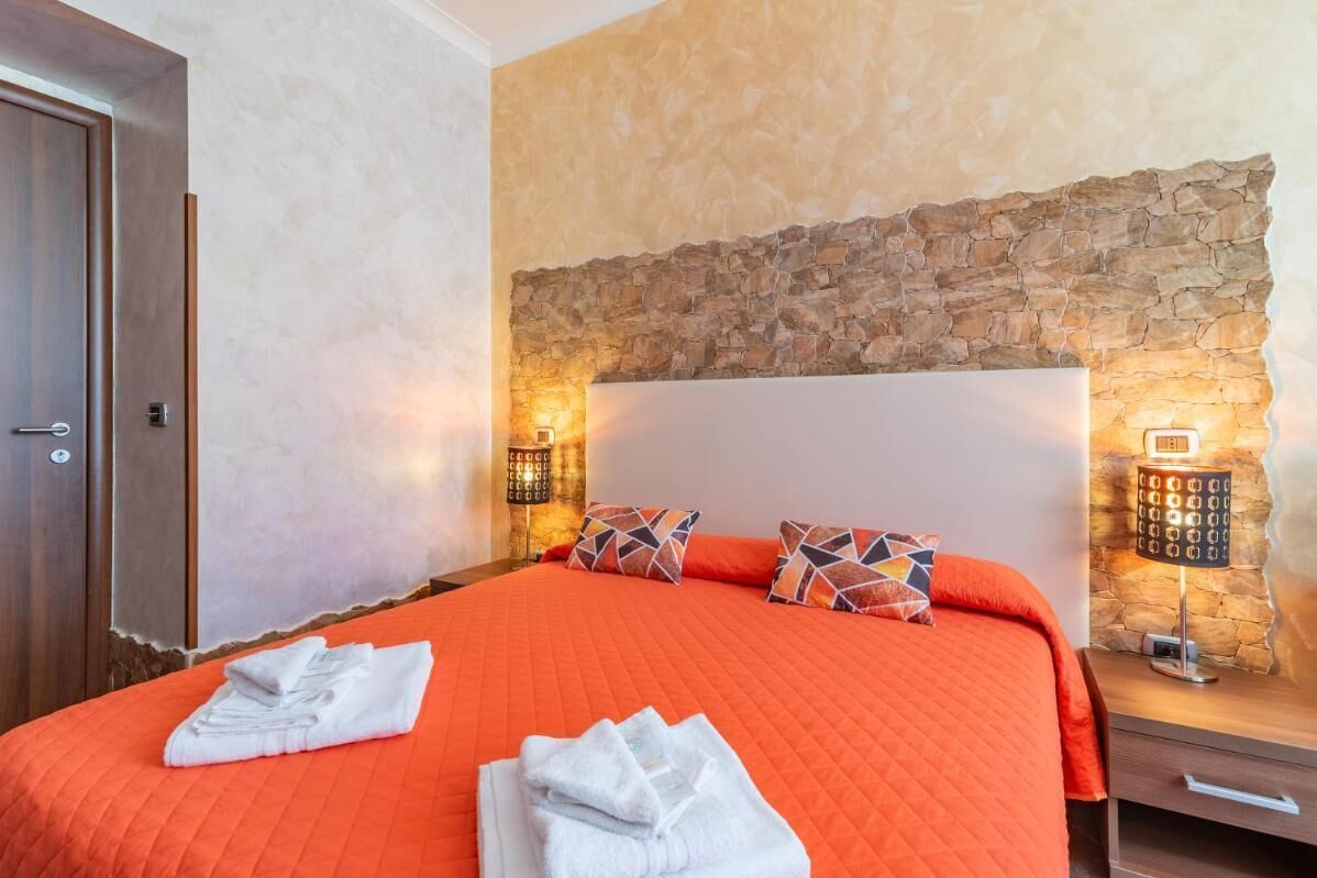 A hotel room with a large bed, a stone wall, and two bedside lamps.
