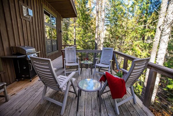A wooden deck with outdoor furniture, a grill, and a view of trees.