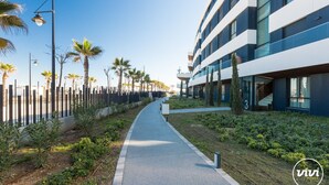 A modern building with a pathway lined with palm trees and a fence. - Galatea | Beachfront - pool - gym (Torremolinos)