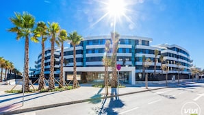 A modern multi-story building with a curved facade, surrounded by palm trees and a clear blue sky. - Galatea | Beachfront - pool - gym (Torremolinos)