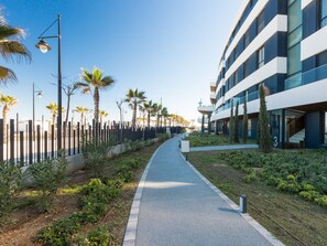 A modern building with a pathway lined with palm trees and a fence. - Galatea | Beachfront - pool - gym (Torremolinos)