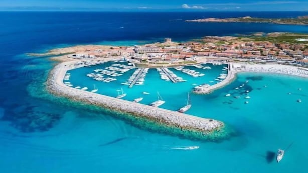 An aerial view of a coastal town with a marina, boats, and a fortified harbor.