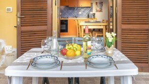 Un espace de restauration en plein air avec une table dressée pour deux personnes, comprenant des assiettes, des couverts, une bouteille et un saladier de fruits.