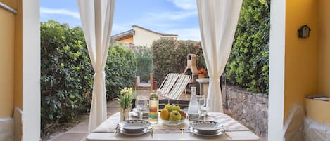 An outdoor dining area with a table set for two, surrounded by greenery and a stone wall.
