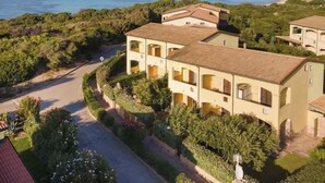 Une villa située sur la côte, dotée de plusieurs balcons, d’une allée pavée et offrant une vue sur la mer et les collines.