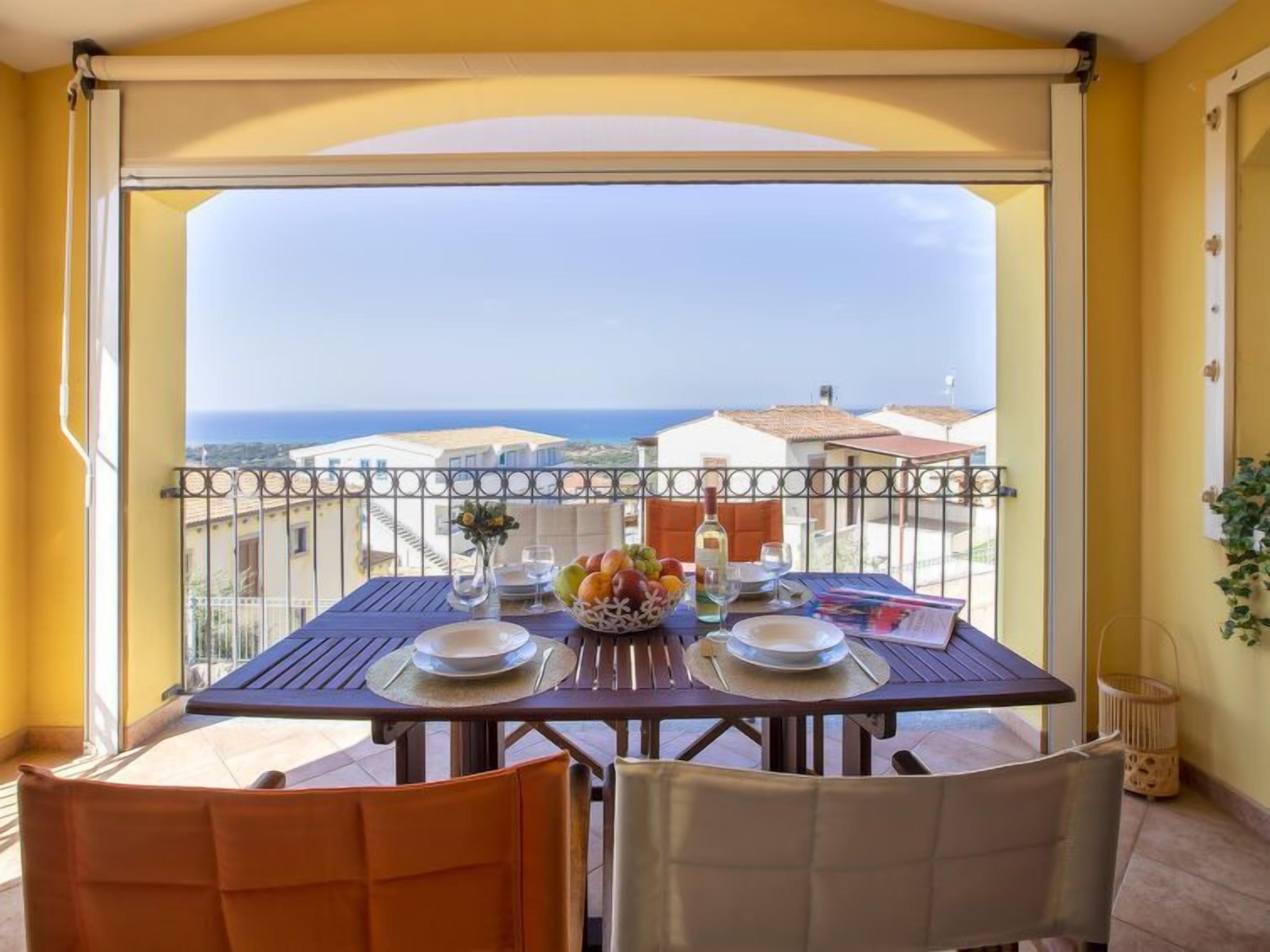 A balcony with a table set for two, overlooking a coastal view.