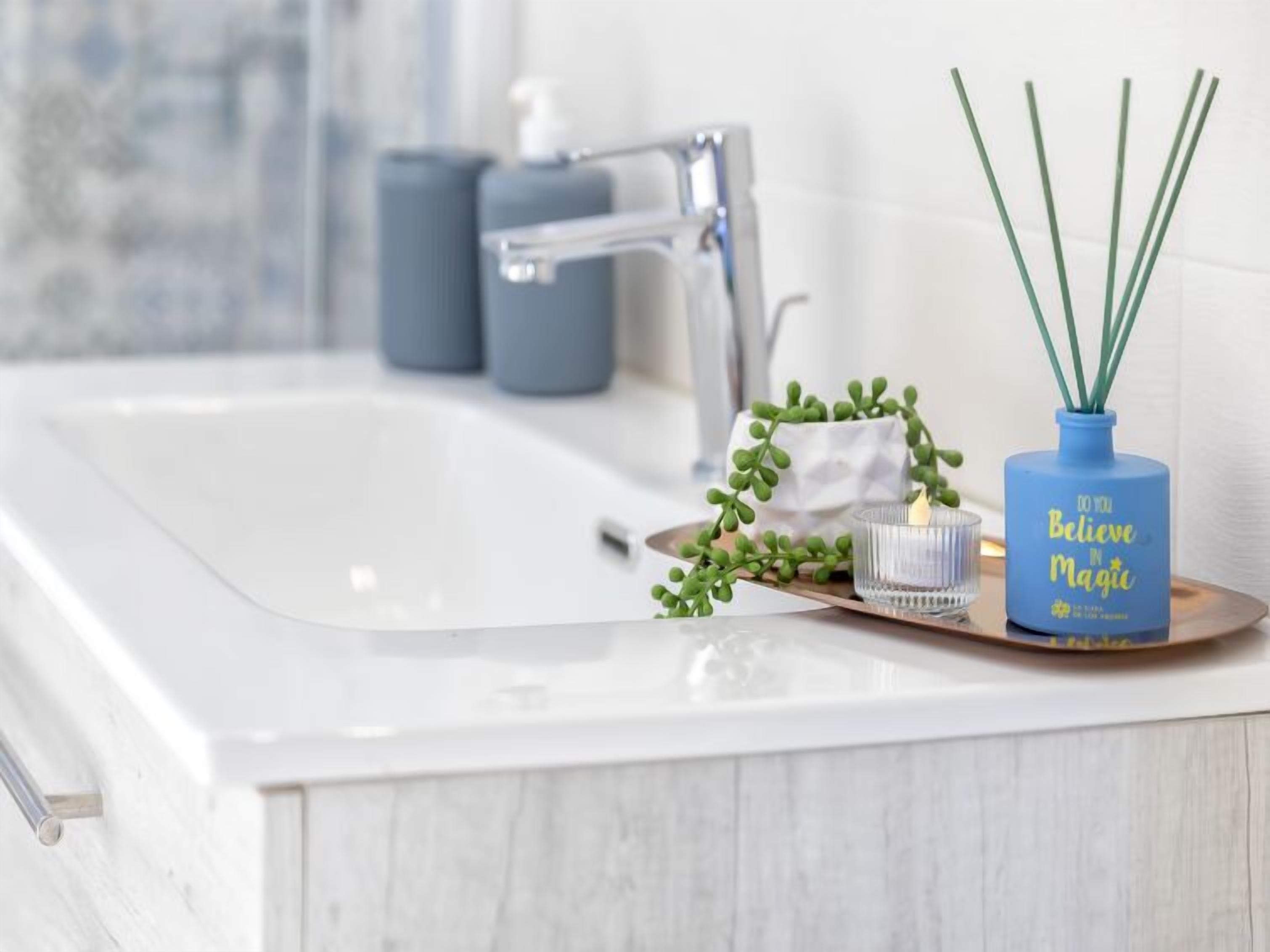 Ein Waschtisch mit weißer Marmorplatte, einem silbernen Wasserhahn und einer blauen Diffusorflasche mit dem Aufdruck "DO YOU Believe in Magic".