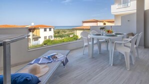 A balcony with a table and chairs, a small sofa, and a view of the sea and neighboring buildings. - Acqua Marina by Interhome (Valledoria)