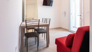 Un coin repas avec une table et des chaises, un téléviseur à écran plat fixé au mur et une chaise rouge.