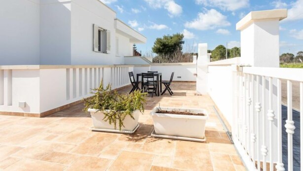 Un bâtiment blanc doté d’une terrasse avec une table et des chaises, des plantes en pot et une balustrade blanche.