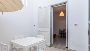 Une pièce blanche avec une table et des chaises, une porte coulissante donnant sur une autre pièce et un luminaire suspendu.