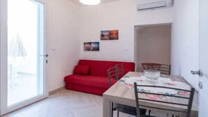 Un espace de vie compact comprenant un coin repas, un canapé rouge et une table recouverte d’une nappe à motifs floraux.