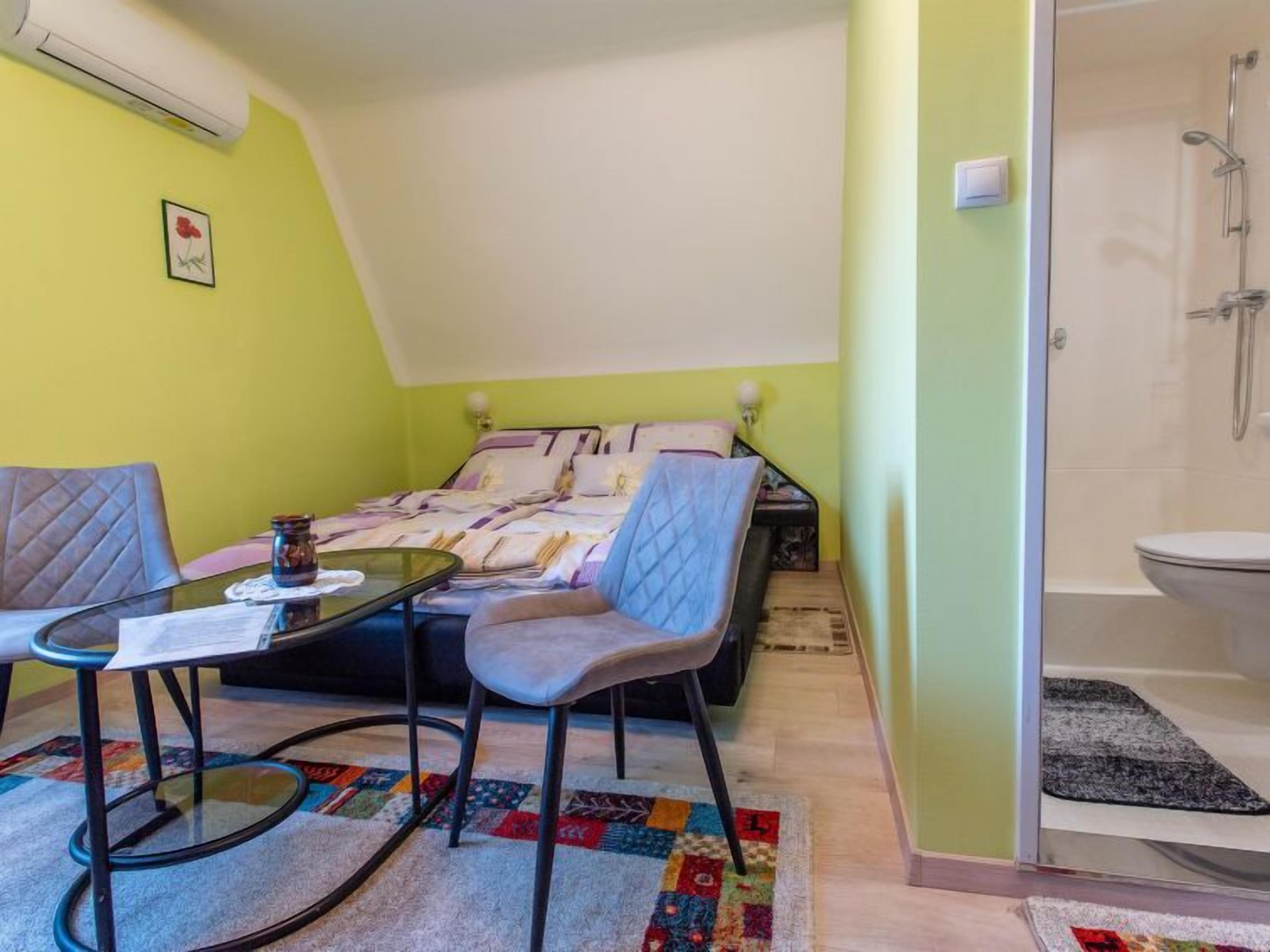 A small, cozy room with a bed, a table, two chairs, and a shower area.