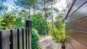 A wooden pathway leading to a building with a brick chimney, surrounded by lush greenery and trees. - Les Landaises by Interhome (Lacanau)