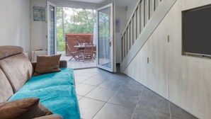 A modern living room with a sofa, a TV, and a sliding glass door leading to an outdoor patio. - Les Landaises by Interhome (Lacanau)