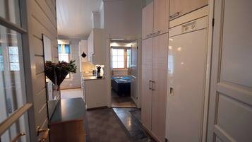 A narrow hallway with a bed in the background, a kitchenette area, and a door leading to another room.