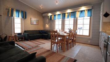 A cozy living room with a sectional sofa, a dining table with chairs, and a kitchen area with a refrigerator.