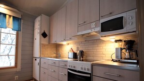 Une cuisine moderne avec des meubles de couleur bois clair, un plan de travail en acier inoxydable, un four encastré, un four à micro-ondes et une machine à café.