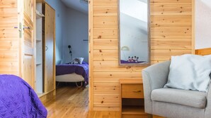 A cozy cabin-style room with wooden walls and floors, a bed with a purple blanket, a gray armchair, and a large mirror reflecting a small picture. - Saarihely b 9 by Interhome (Inari)