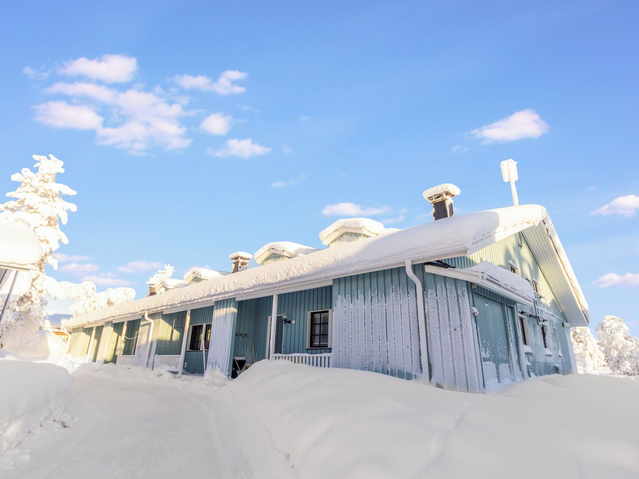 Une maison en bois recouverte de neige, avec plusieurs cheminées et une véranda.