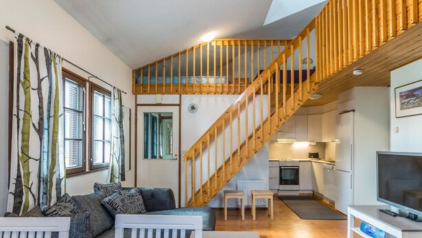 A cozy living room with a wooden staircase, a sofa, a coffee table, and a TV. - Saarihely b 9 by Interhome (Inari)