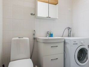 Casa de banho com sanita, lavatório, espelho e máquina de lavar roupa.