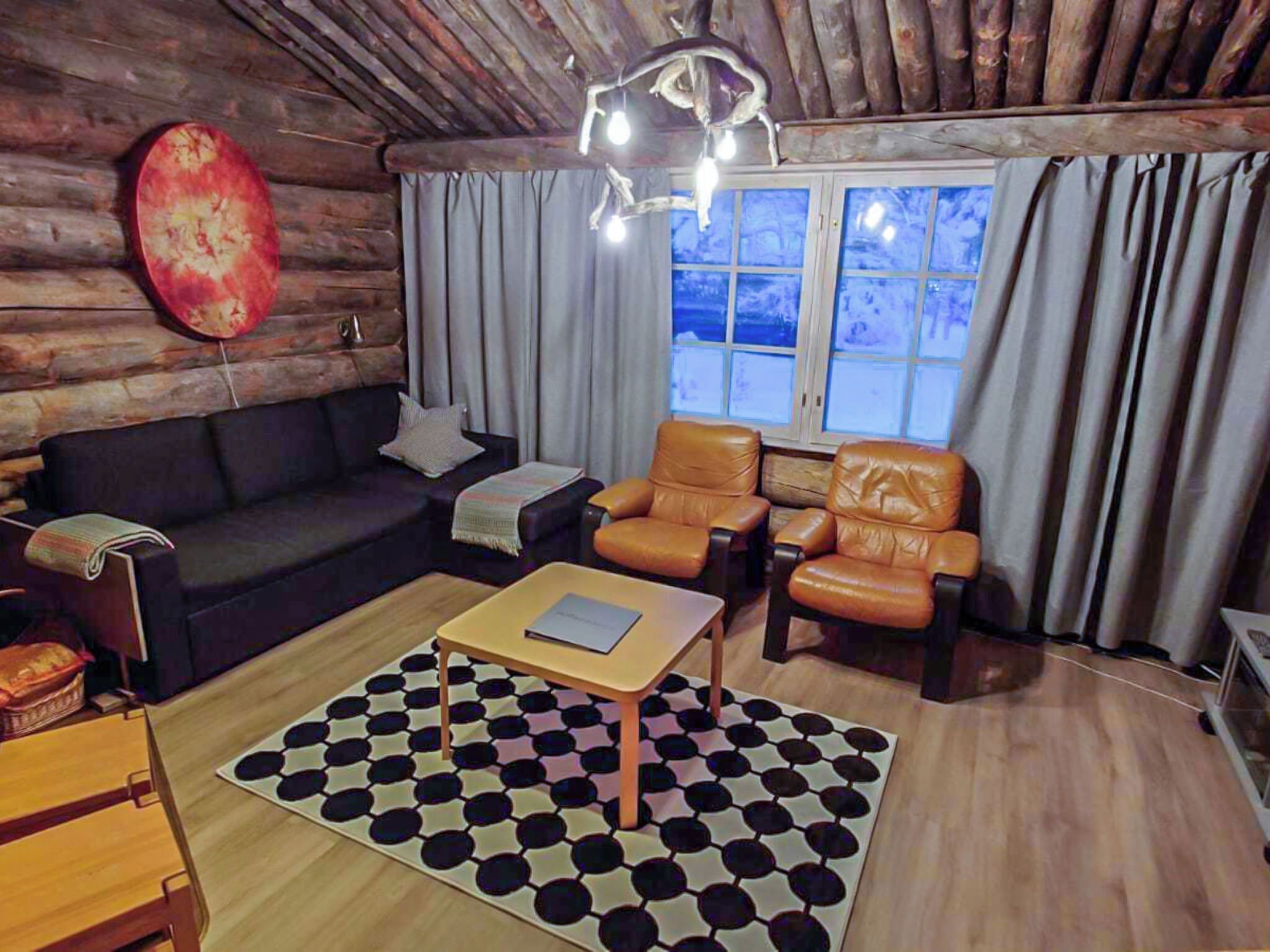 Interior acogedor de una cabaña de madera con un sofá de cuero oscuro, dos sillones de cuero, una mesa de centro de madera y una alfombra estampada.