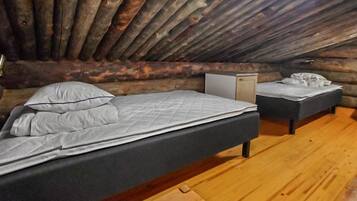 Un dormitorio tipo cabaña de madera con dos camas, un pequeño aparador blanco y suelo de madera.