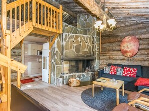 L’intérieur chaleureux d’un chalet avec une cheminée en pierre, un escalier en bois et un espace de vie comprenant un canapé et une table basse.