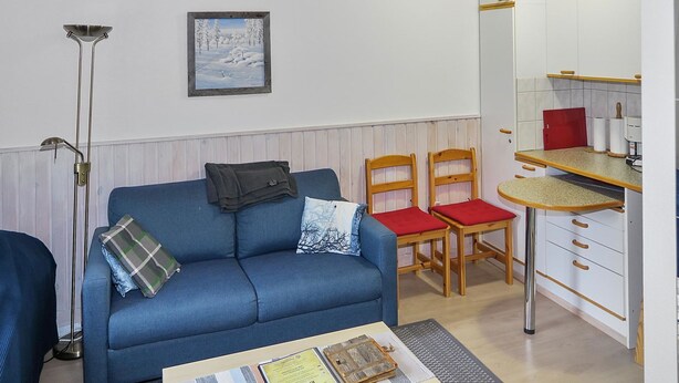 Un espacio habitable compacto con sofá, sillas, una mesa de comedor, kitchenette y una lámpara de pie.