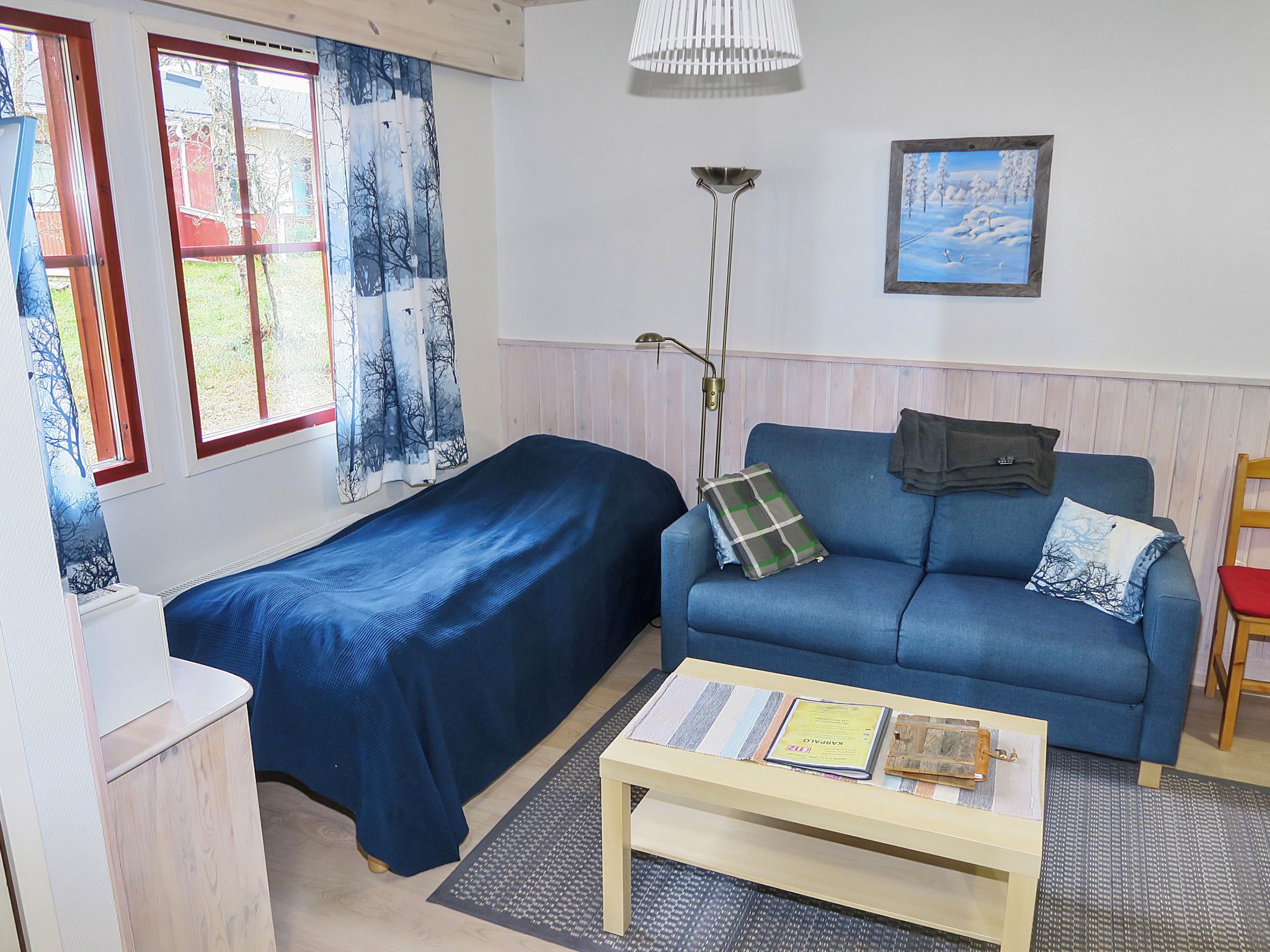 A room with a bed, a sofa, a table, a lamp, and a painting on the wall.