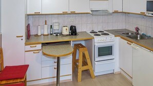Une cuisine compacte avec des meubles blancs, une cuisinière, un évier et un tabouret de bar.