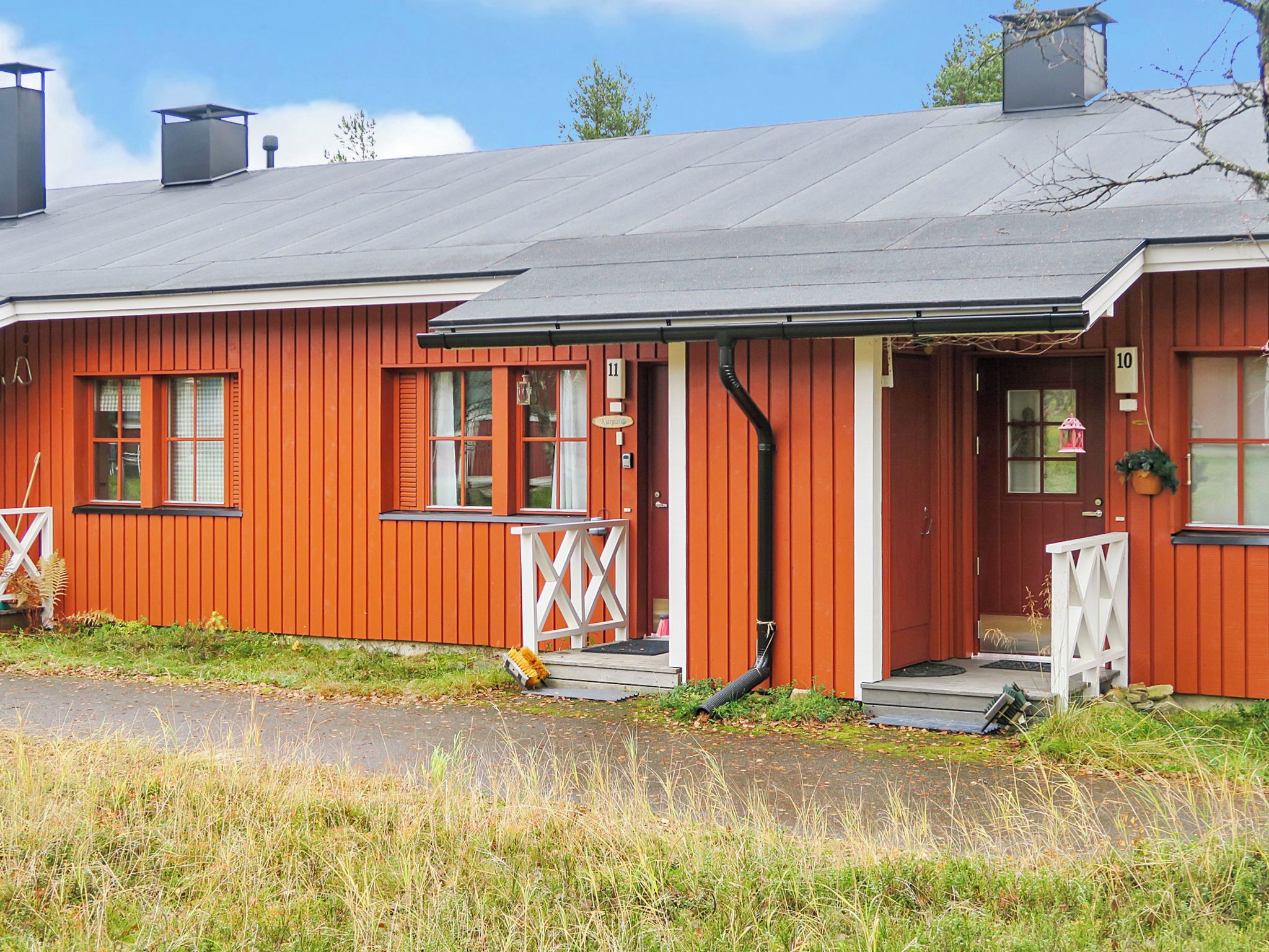 Une maison en bois rouge avec un porche, portant le numéro 11, et un petit jardin devant.