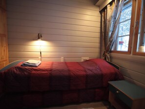 Un dormitorio con cama, mesita de noche, lámpara y ventana con cortinas.