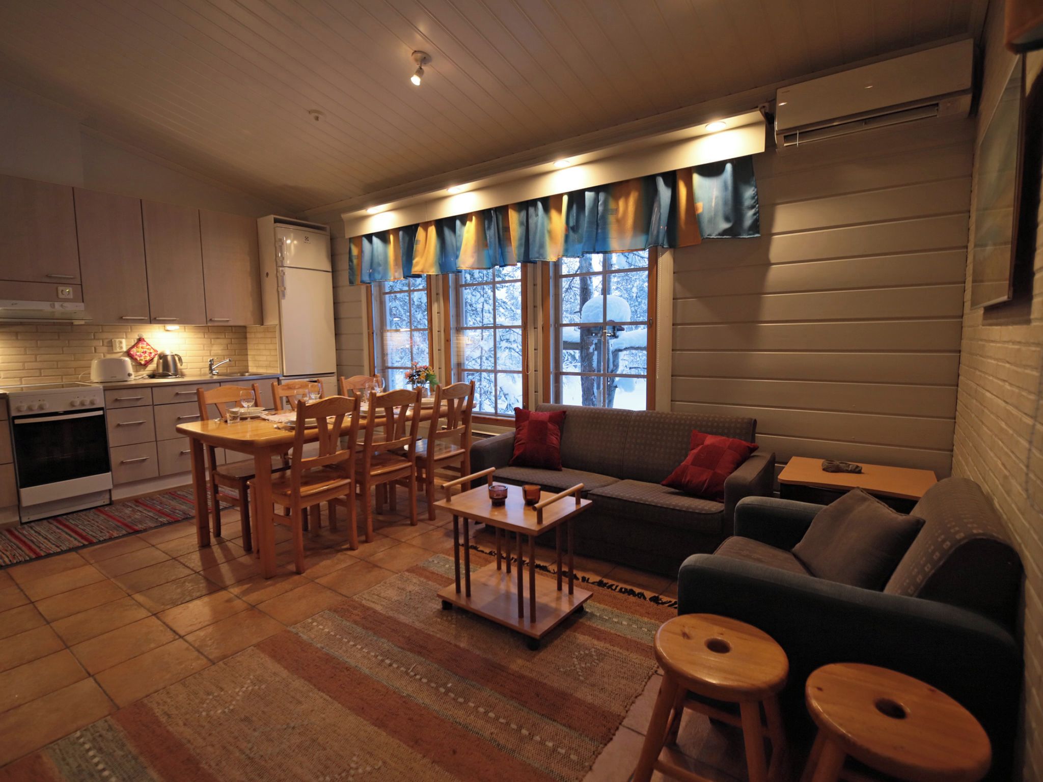 Un salon chaleureux avec un coin repas, des meubles en bois et une vue sur un paysage enneigé grâce à de grandes fenêtres.