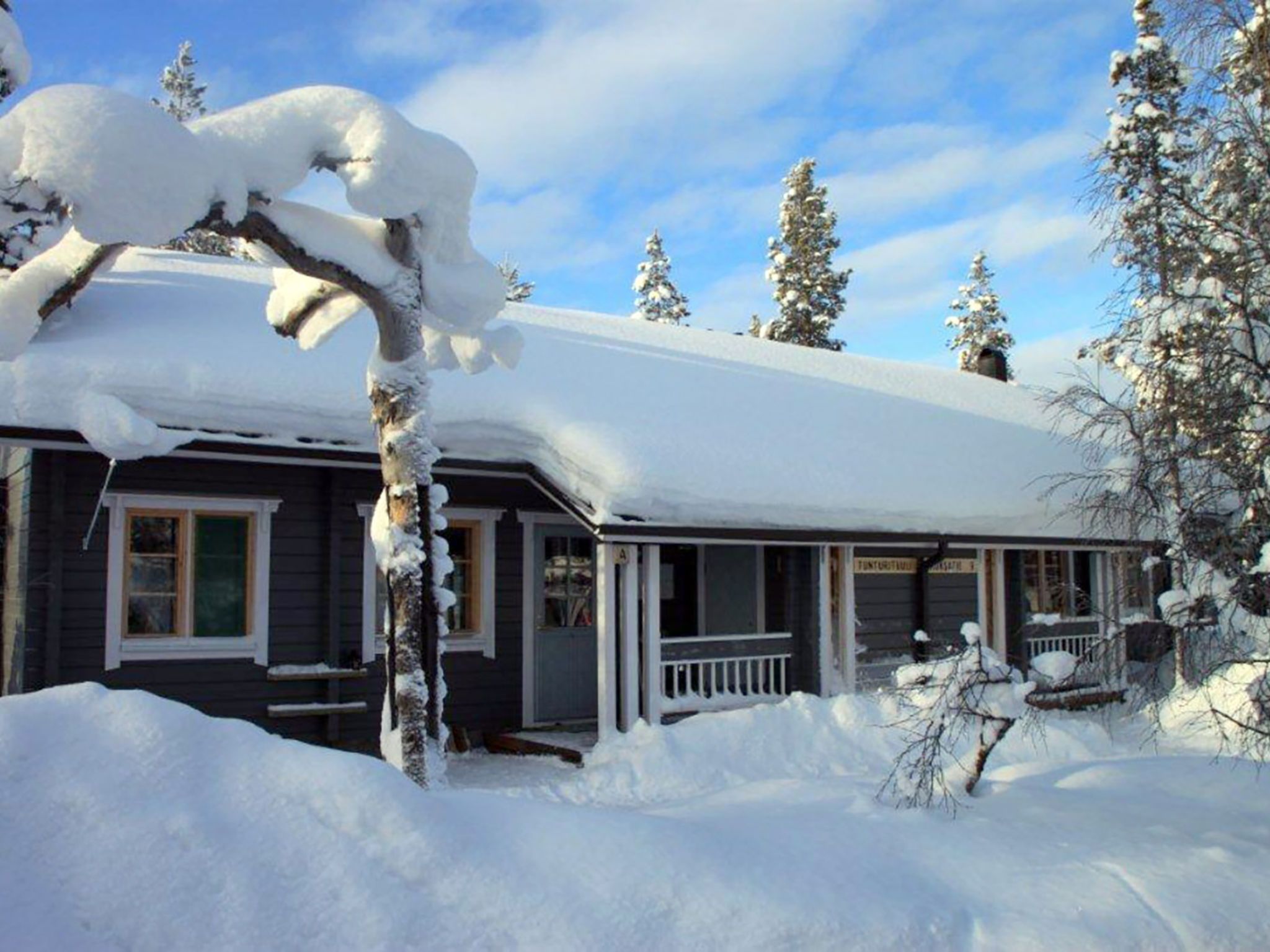 Ein mit Schnee bedecktes Haus mit einer Veranda und blauem Himmel.