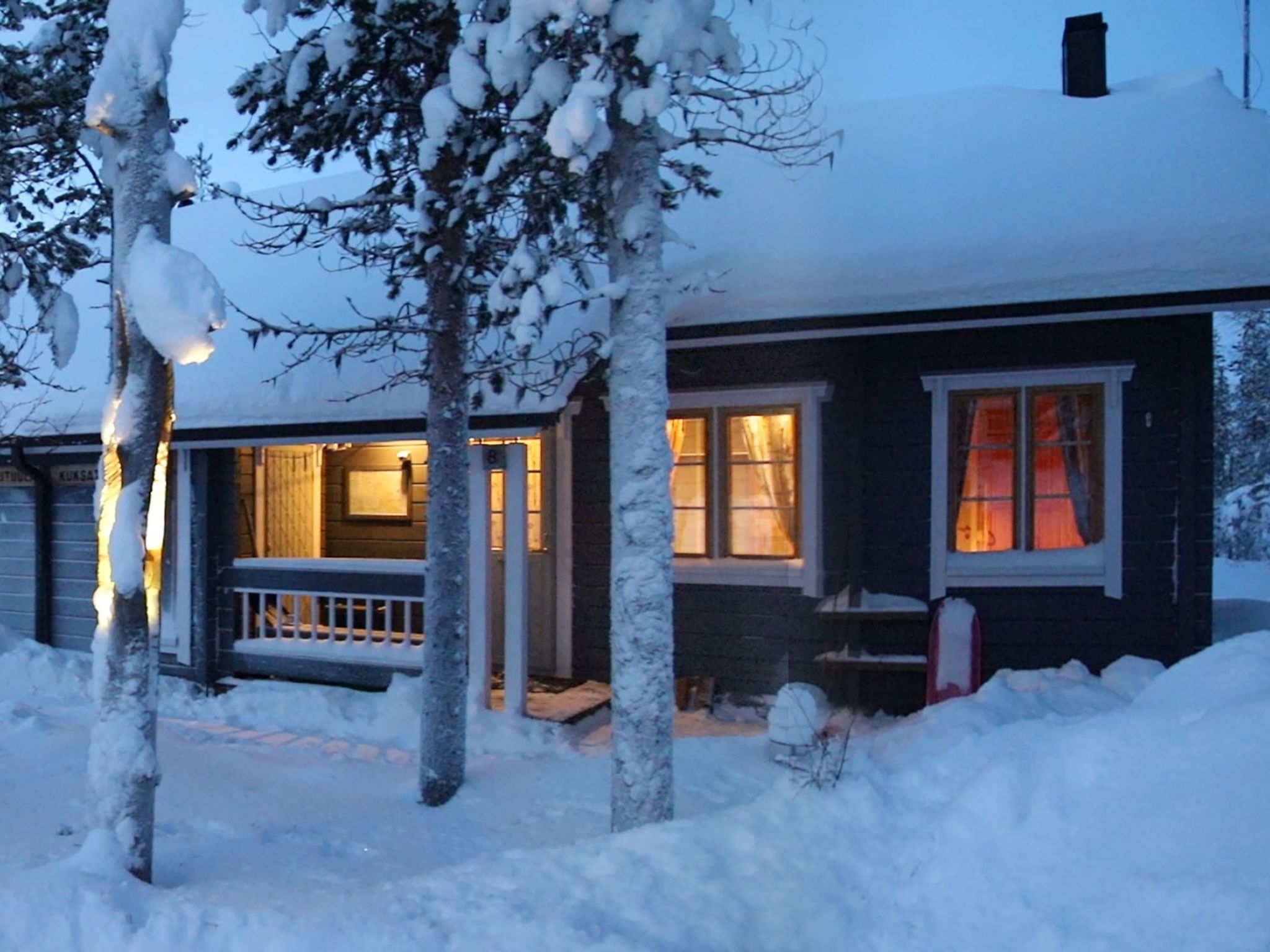 Une maison recouverte de neige, avec un porche et un intérieur éclairé.