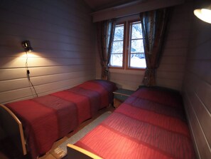 Habitació amb dos llits, una finestra amb cortines i una làmpada penjada a la paret.