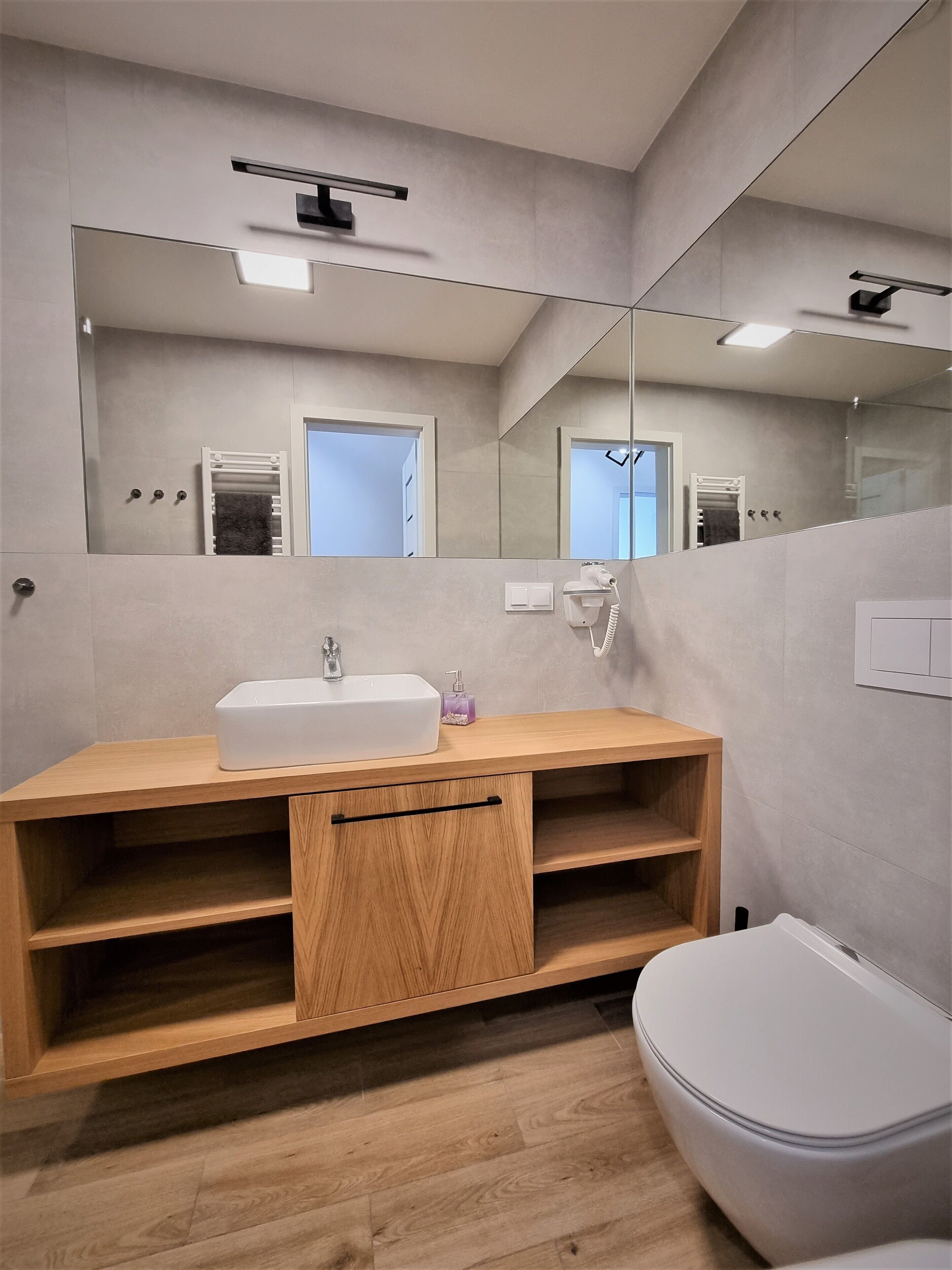 A modern bathroom with a wooden vanity, a white sink, a mirror, and a toilet.