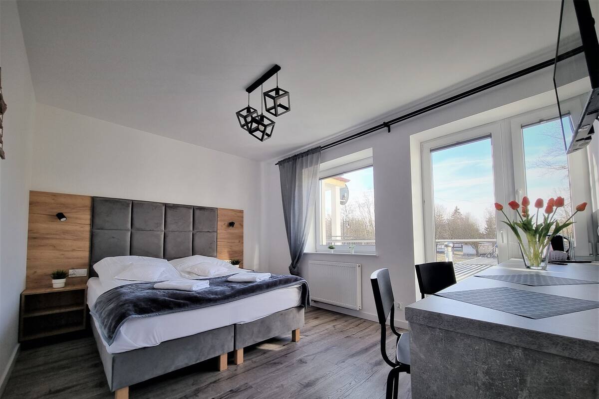 Une chambre moderne avec un grand lit, un bureau avec un ordinateur portable et une fenêtre donnant sur l’extérieur.