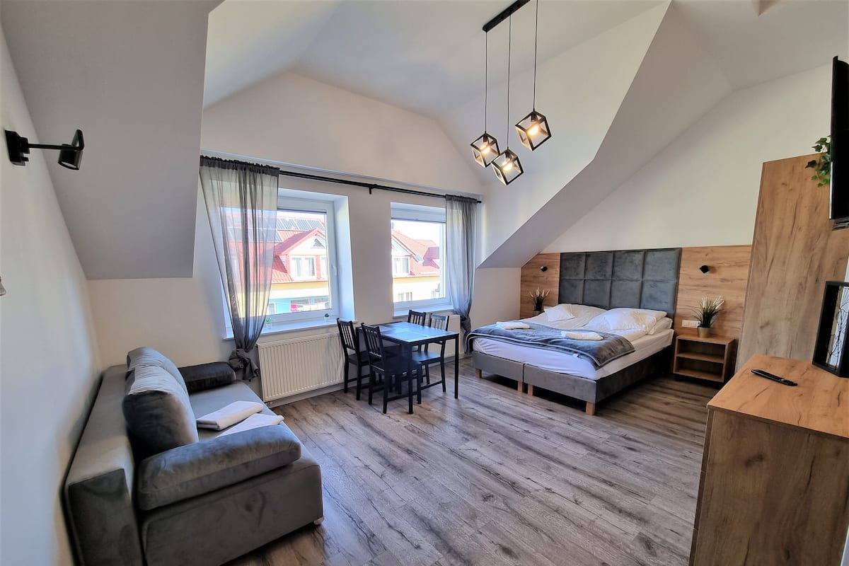 Une chambre de style loft moderne, avec un plafond en hauteur, un lit, un canapé, une table à manger et un petit coin cuisine.