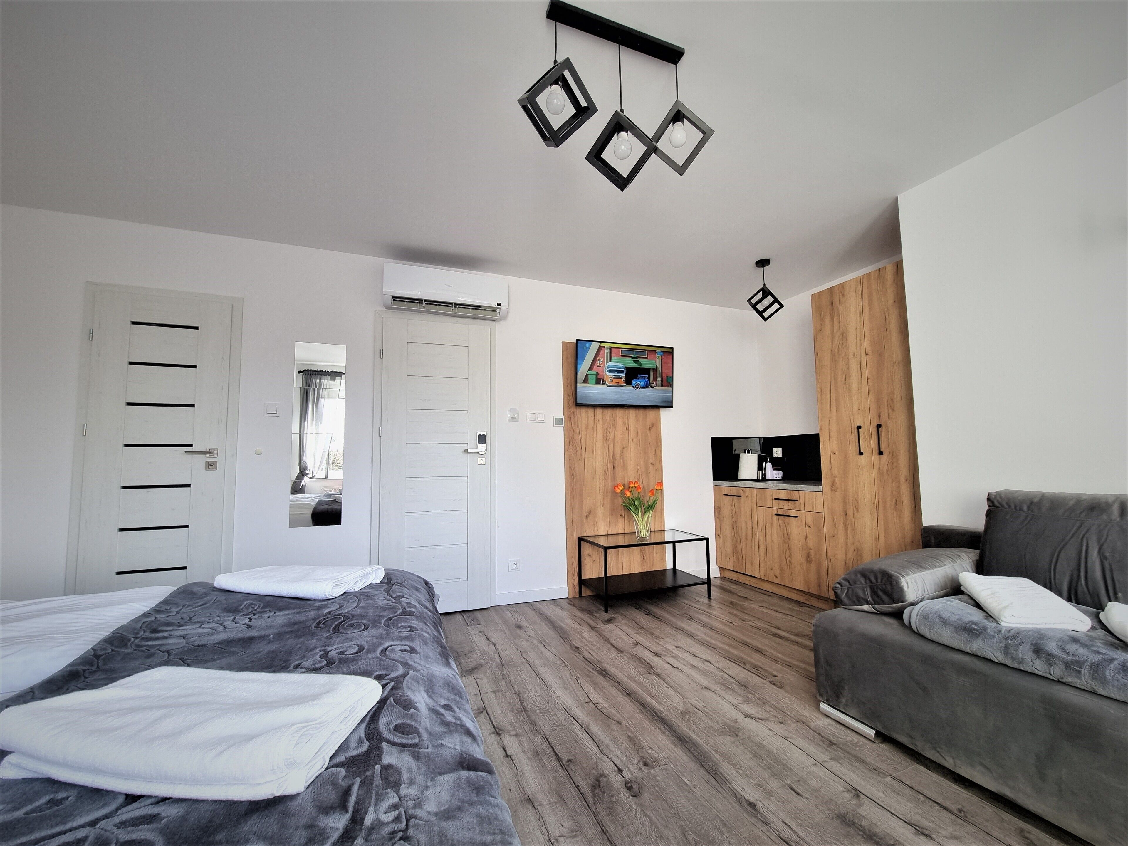 Ein modernes Schlafzimmer mit einem Bett, einer Couch, einem Fernseher und einem Holzschrank.