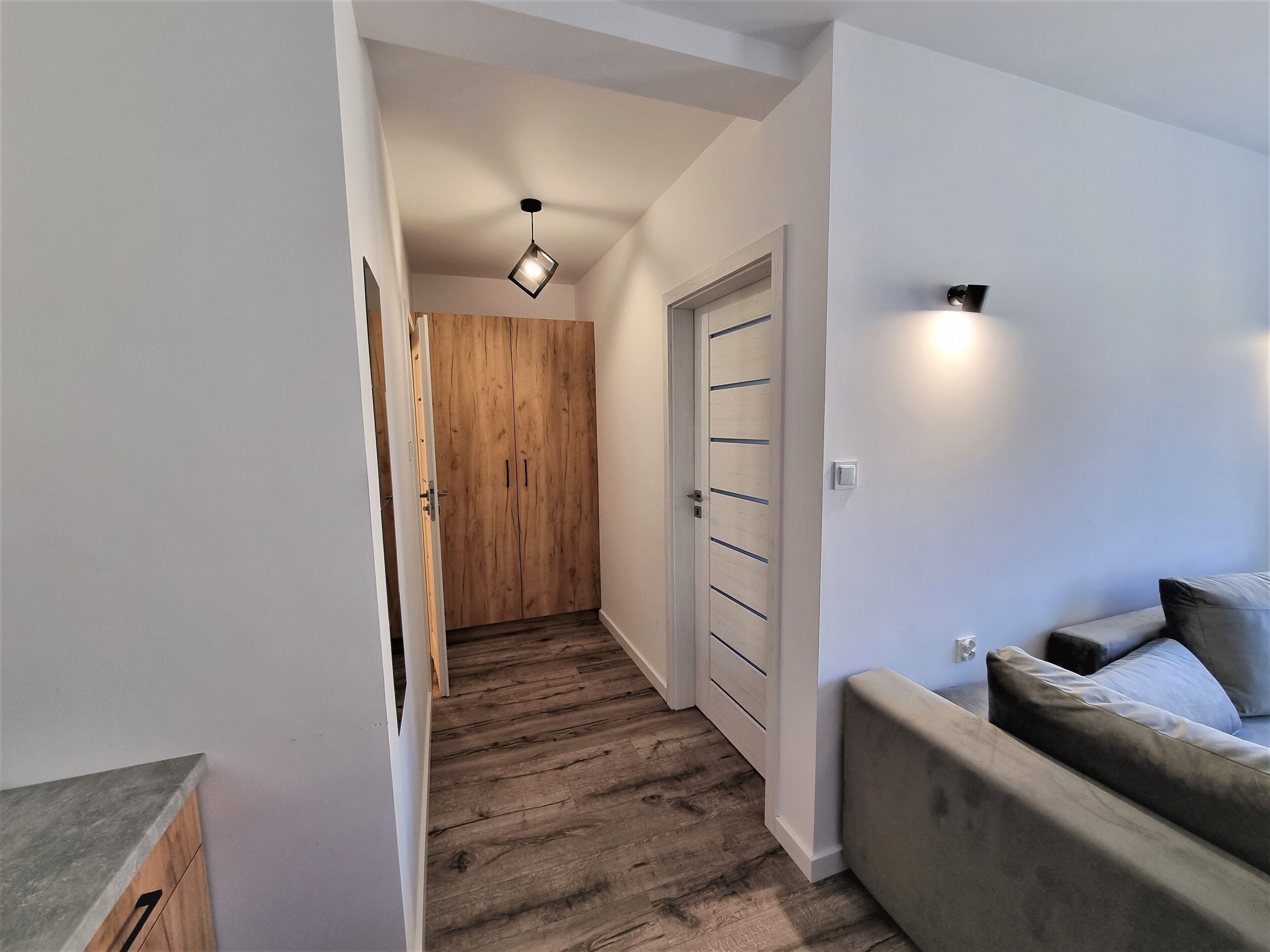Un couloir avec une armoire en bois, un lit avec une tête de lit et un luminaire fixé au mur.