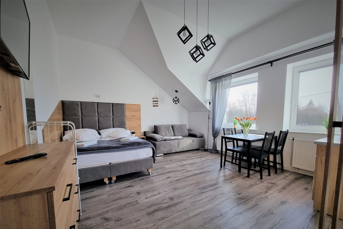 Une chambre moderne avec un lit de style industriel, un coin repas et une grande fenêtre.