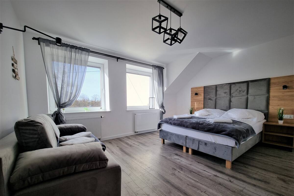 Une chambre moderne avec un lit, un canapé et une fenêtre ornée de rideaux légers.