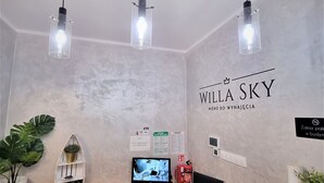 A reception desk with a wooden finish, a mounted flat-screen TV, and a wall-mounted fire extinguisher. - Willa Sky (Wladyslawowo)