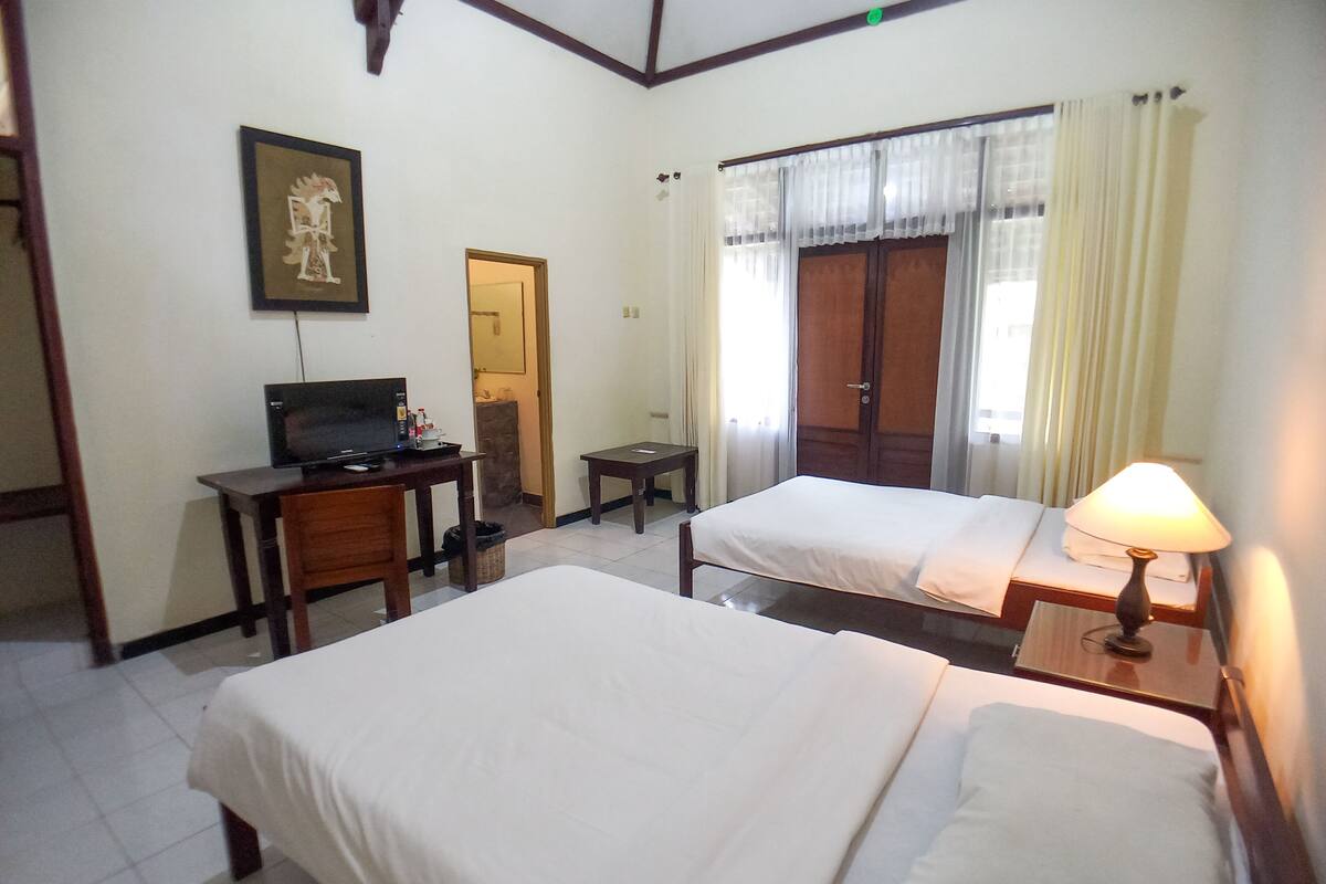 A hotel room with two beds, a desk with a computer, a television, and a lamp.