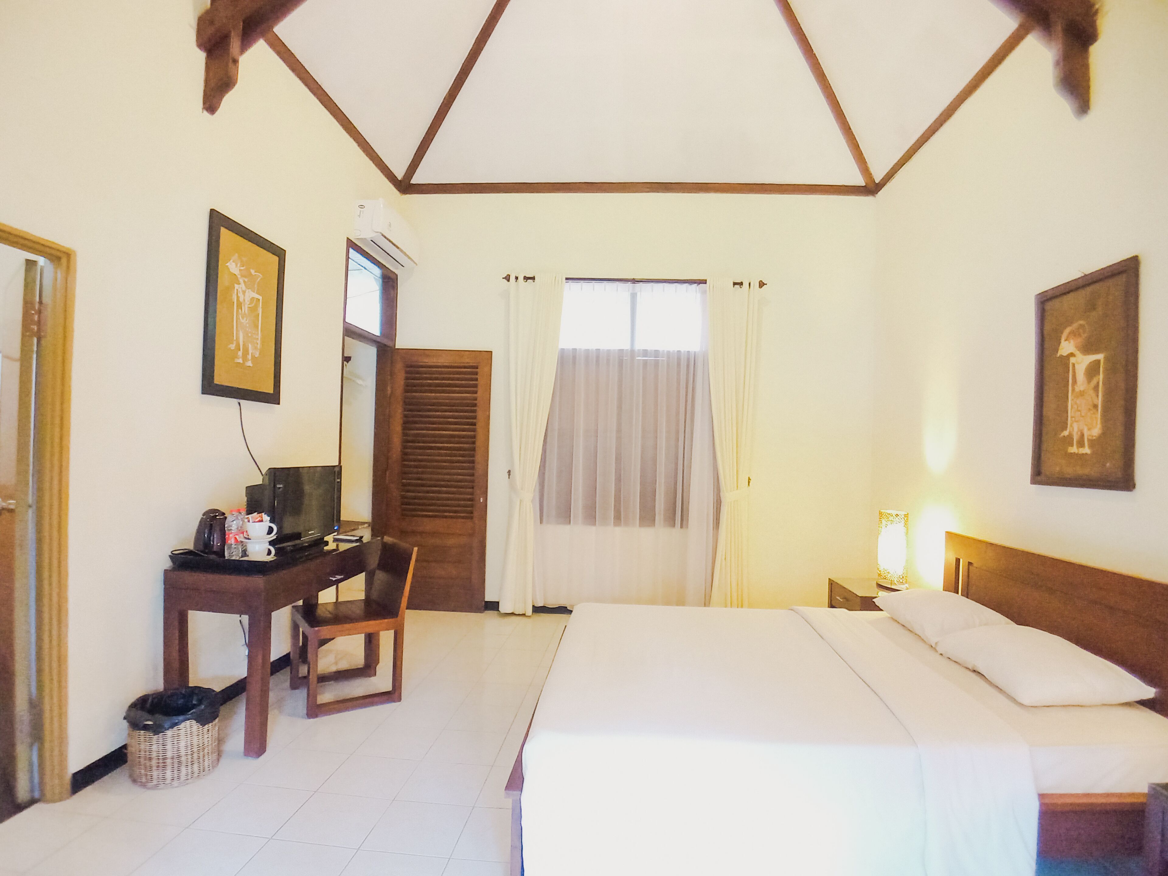 A hotel room with a bed, a desk with a chair, a television, and a window with curtains.