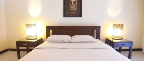 A neatly made bed with white linens, two bedside tables with lamps, and a framed artwork above the bed.