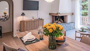 Un comedor con una mesa de madera preparada para dos personas, un florero con flores amarillas y una chimenea al fondo.